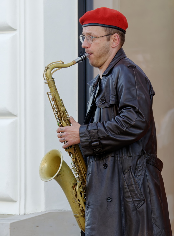 3 - Person playing a vintage saxophone while wearing a black leather trench coat and a distinctive red beret